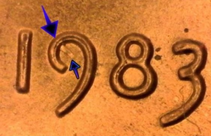 microscopic image of the 1983 date of a of a one cent penny worth money with arrows noting the struck through error on the 9 of the date